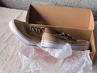 Pair of tan Vans sneakers placed in original cardboard shoe box with Vans tissue paper.