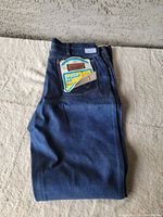 Folded dark blue denim jeans showing back pocket with leather Wrangler patch and paper tag for regular fit boot jean.