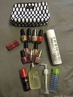 Photo of the cosmetics lot showing seven OPI nail polishes in various colors, two pink lipsticks, hair energizer spray can, Calvin Klein cologne bottle, clear pump bottle, styling product bottle, and a mariposa cosmetic bag.