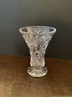 Photo of a clear cut glass vase with diamond pattern on a brown surface against a black background.