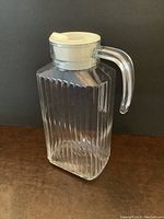 Glass juice pitcher with vertical ribbed Deco style design, clear glass, plastic lid closed on top.