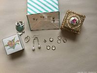 Photo shows assortment of stud and hoop earrings alongside painted ceramic and gold-tone metal jewelry boxes.