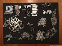 Overview of mixed silver-colored metal jewellery findings including tubes, rings, chains, clasps, and small small beads and washers.
