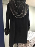 Rear view of black faux suede ladies coat showing removable hood with dark brown faux fur lining and sleeve cuffs.