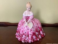 Front view of Royal Doulton bone china Victorian-style figurine of seated girl holding fan in pink floral dress.