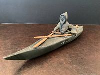 Front side angle view of Inuit hunter seated in kayak holding paddle and harpoon.