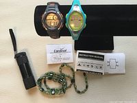 Photo showing two digital sports watches, their instruction manuals, a green and black magnetic wrap bracelet, and a small black flashlight with a wrist strap.