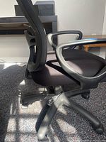 Side view showing chair seat, mesh back, fixed plastic armrest and five-legged plastic base with casters.