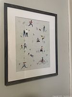 Photo of framed picture showing multiple human figures in movement against a light background, framed in dark wood with white mat.