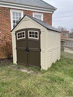 Exterior view of tan and brown Suncast shed positioned against brick wall