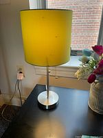 Full view of the 17 inch tall brushed nickel table lamp with yellow shade on a desk near a window.