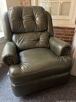 Front view of olive-green leather recliner chair with padded button-tufted backrest and armrests, showing nailhead trim detail and cushion condition.