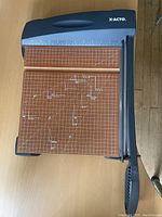 Top view of the paper cutter showing the wood base with white grid and measurement markings and black cutting arm with the X-ACTO logo on the housing.