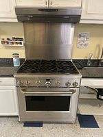 Full frontal view of stainless steel gas range installed under matching range hood within kitchen cabinetry.