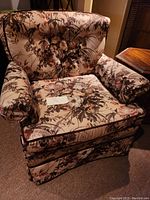 Front angled view of floral upholstered armchair showing padded armrests, tufted backrest, and seat cushion