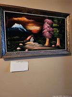 Framed landscape painting with house, snow-capped mountain, two large trees (one pink, one green), and a glowing sun in a dark sky