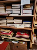 Shelves filled with a variety of books including hardcover, paperback, and notebooks. Some books are stacked horizontally while others are upright. A handwritten sign indicates a section labeled 'books 1-12'.