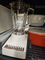 Photo of a white kitchen blender with a clear glass jar and multiple speed buttons on the base, placed next to some containers.