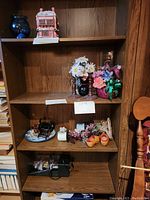 Shelves of large dark wood bookshelf with assorted decorative items: blue vase, pagoda piece, flower arrangements, miniature sewing machine, decorative shoes.