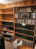 Photo showing two wooden book shelves filled with books, DVDs, VHS tapes, records and other media items