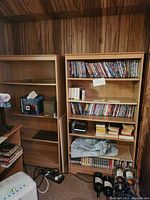 Two tall wooden book shelves standing side by side. One shelf is empty while the other contains DVDs and other items, which are not included.