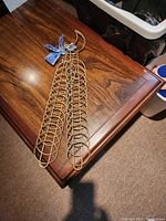 Photo of gold metal Christmas card holder on a wooden table, showing circular loops for holding cards and blue fabric bow at top.
