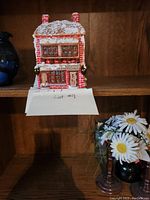 Front view of the Christmas decorative house figurine showing red brick walls, snowy roof, and decorated windows.