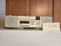 Front view of beige under-cabinet mountable clock radio with dual speakers, digital time display, and control buttons.