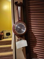 Front view of wooden wall decoration with round compass and vertical thermometer above it