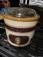 Small crockpot slow cooker showing the ceramic body with striped design and the glass lid on top.