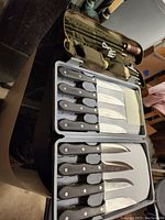 Overview of six fixed blade knives in plastic case alongside green army cleaning kit pouch with cleaning rods and brushes.