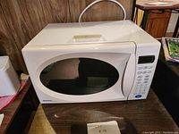 White Emerson microwave oven showing front and side top view with numeric keypad and display.