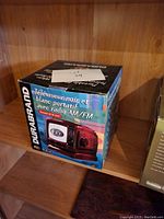 Box of Durabrand portable black and white TV combined with AM/FM radio seen on a wooden shelf.