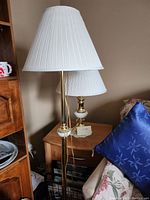Three brass and ceramic table lamps shown together, two smaller matching lamps and one taller lamp with white pleated shades.