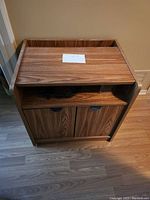 Front view of the small durable cabinet showing the wood grain finish, open shelf area with compartments, and two lower doors with black recessed handles.