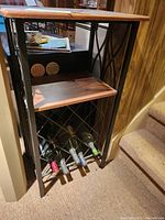 Photo of a small wood and black metal table with two shelves and a lower built-in wine rack holding six wine bottles.