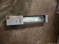 Photo of new 18 inch towel bar in original Yorkshire Monroe packaging with brass finish, lying on concrete floor.