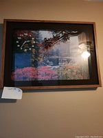 Photo of framed wall art showing a forest scene with autumn colors and an integrated analog clock in the upper left corner.