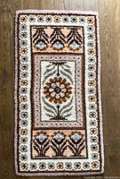 Full view of the rectangular handmade rug showing the overall floral and geometric pattern in tan, brown, blue, white, and beige colors on wooden floor.