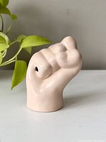 Front angled view of the pink ceramic hand balloon holder showing smooth glazed surface and hole on the side.
