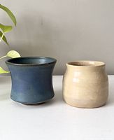 Pair of small pottery vases side by side on a white surface under natural light.