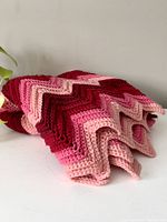 Folded pink wool throw blanket showing zigzag crochet pattern in shades of pink and red.