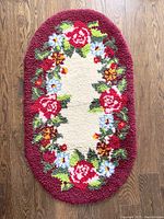 Top view of the oval rug on wood floor showing red floral border pattern and cream center