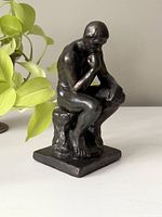 Front angle of the thinking man sculpture next to a houseplant for scale.