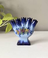 Front view of vintage ceramic vase showing five finger-shaped openings and floral hand-painted design in blue, white, pink, and yellow.