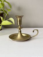 Side view of the vintage brass chamber-style candlestick holder showing the handle and overall shape.