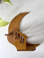 Front and side view of vintage wooden crescent moon shaped hanging shelf with small house cutout and brass bars on windows.