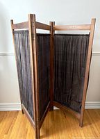Full view of the vintage wooden room divider showing the three folding panels with dark patterned fabric stretched within the wooden frame.