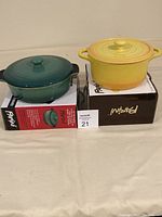 Yellow flameproof ceramic casserole pot with lid on top of its original Parini box next to the green round ceramic bakeware with lid also on its original Parini box.