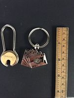 Silver and gold tone Harrods key holders displayed on black background with ruler for scale